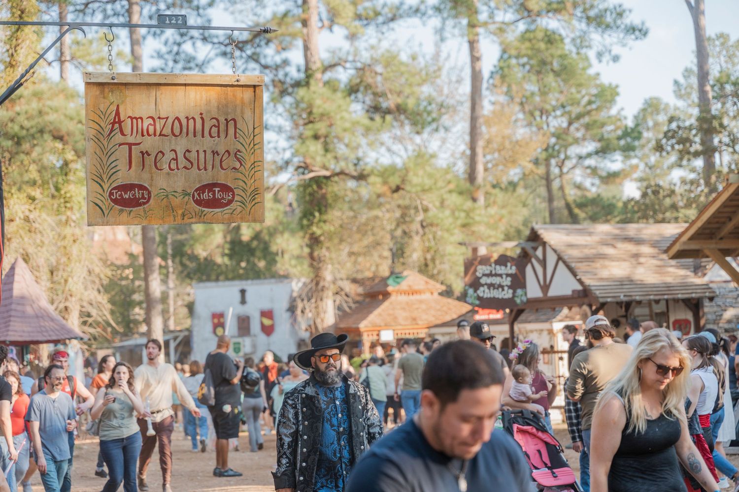 A crowded pathway at a renaissance festival with Amazonian Treasures shop sign visible.