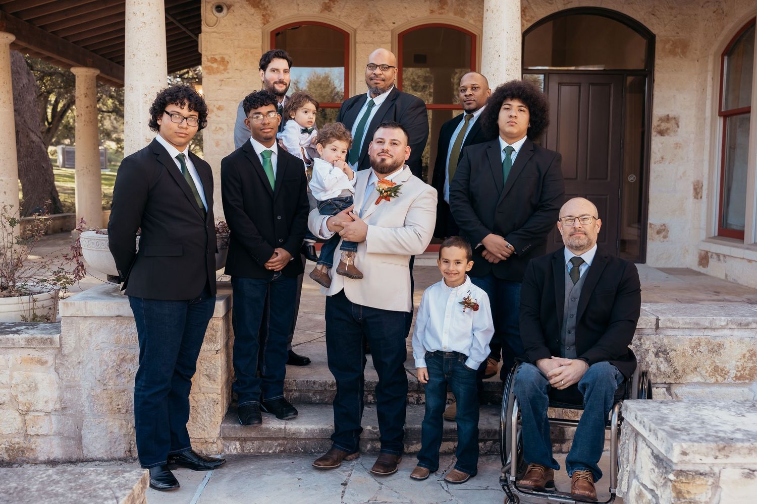 Group portrait of wedding party members on stone steps with arched doorways.