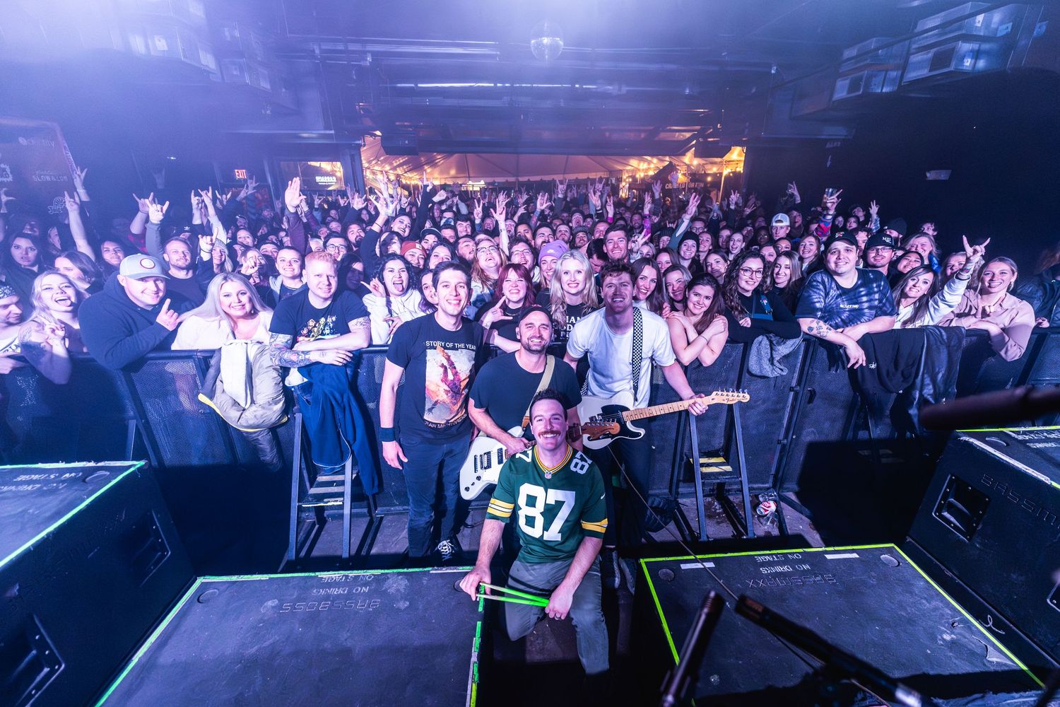 Packed concert venue showing enthusiastic crowd from stage perspective with blue lighting.