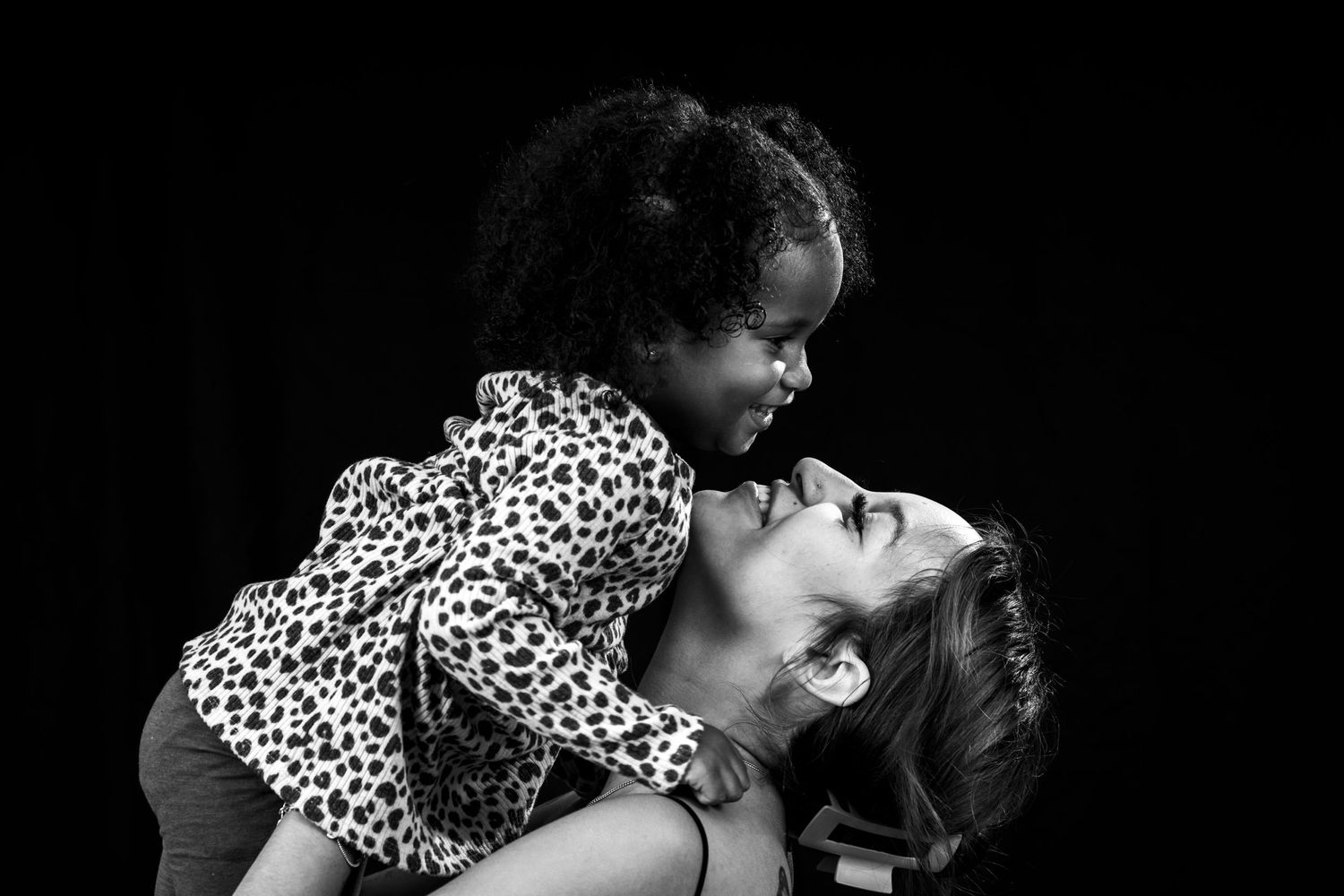 Artistic black and white photo capturing playful moment between child and woman.