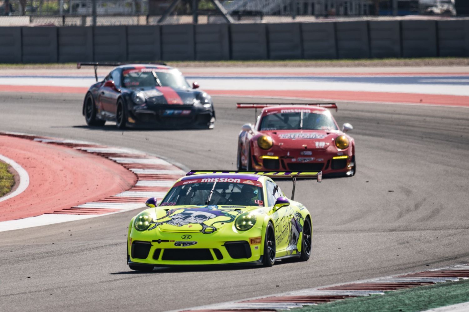 Three GT race cars compete through a corner, with a lime green Porsche in front.