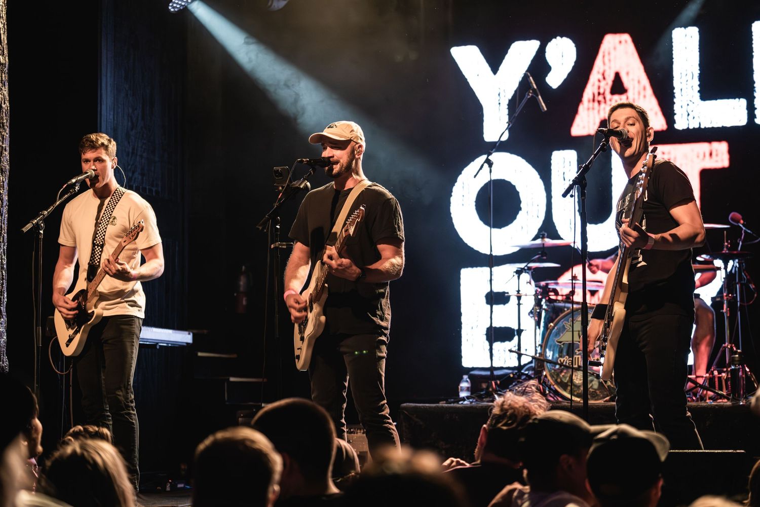 Rock band performs on stage with 'Y'ALL OUT' illuminated sign and dramatic lighting.