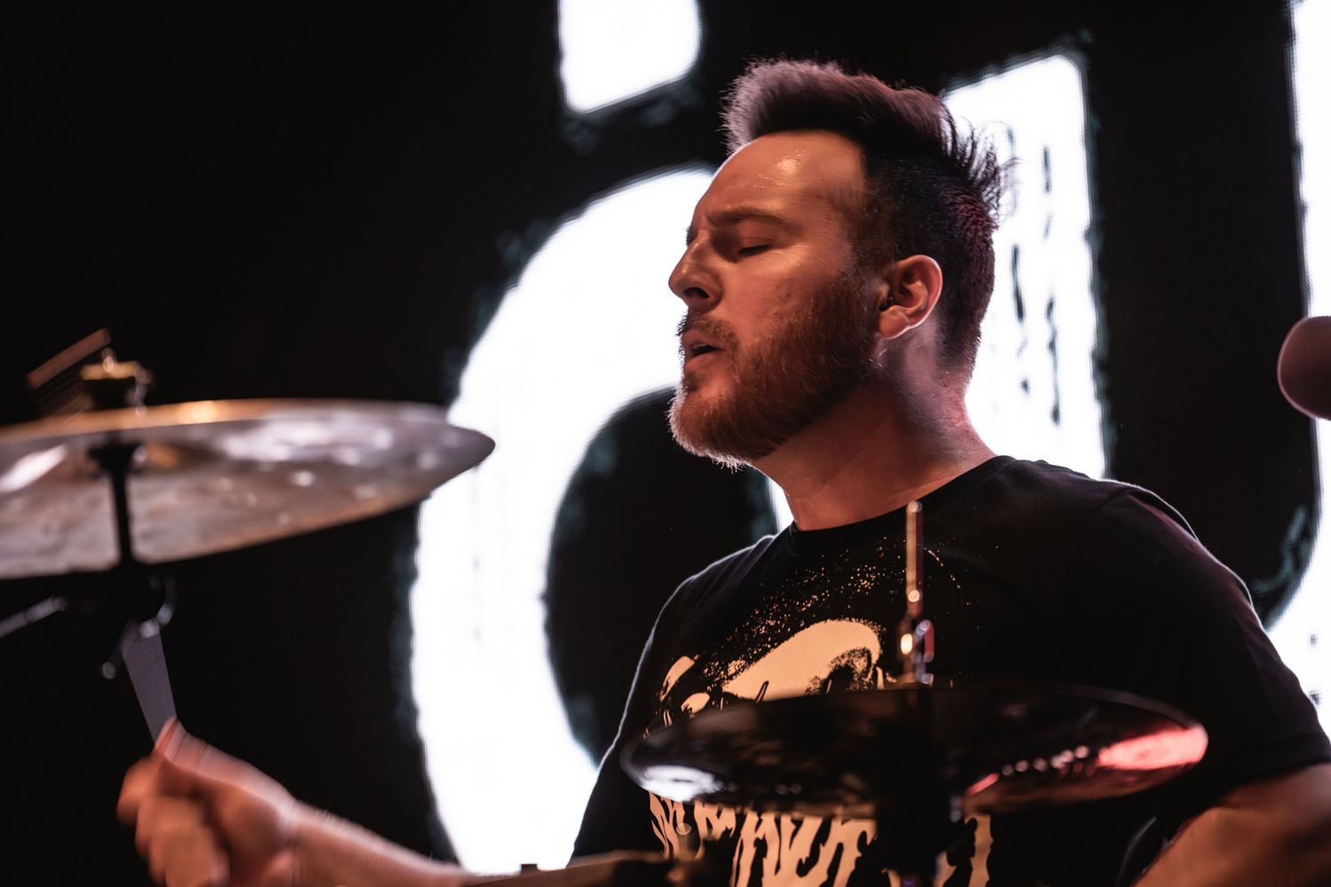 Drummer performs passionately during live concert with spotlights.