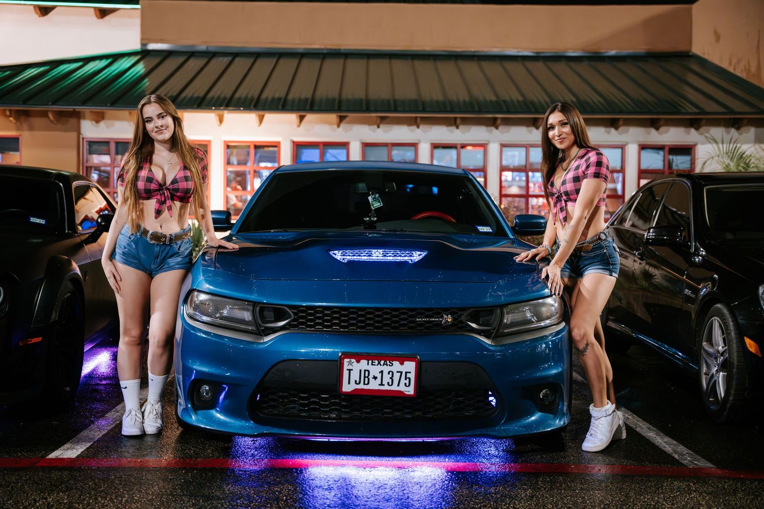 Blue Dodge Charger with LED underlights parked in front of a retail storefront at night.