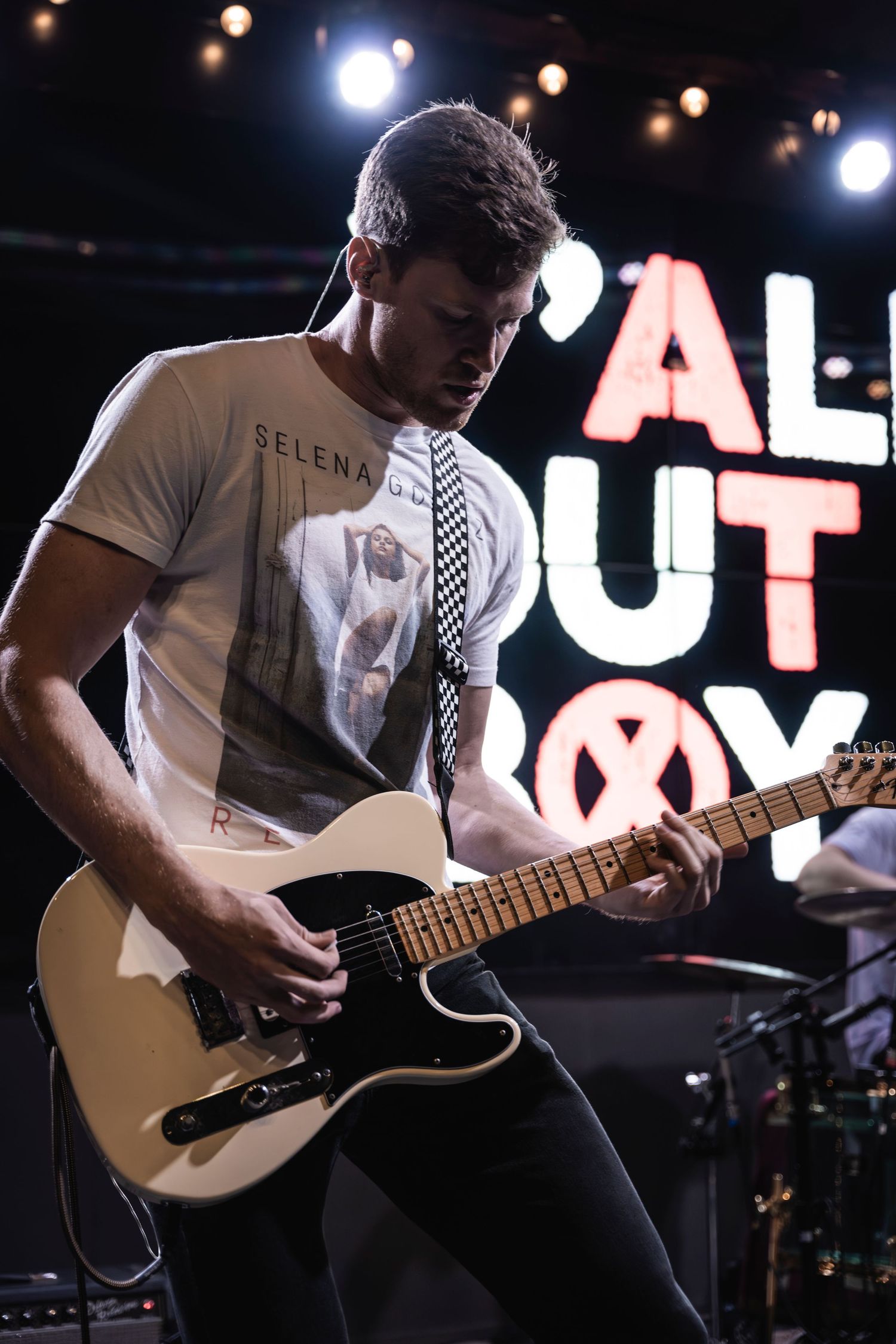 Guitarist performs with cream Telecaster guitar against illuminated 'ALL OUT' signage.