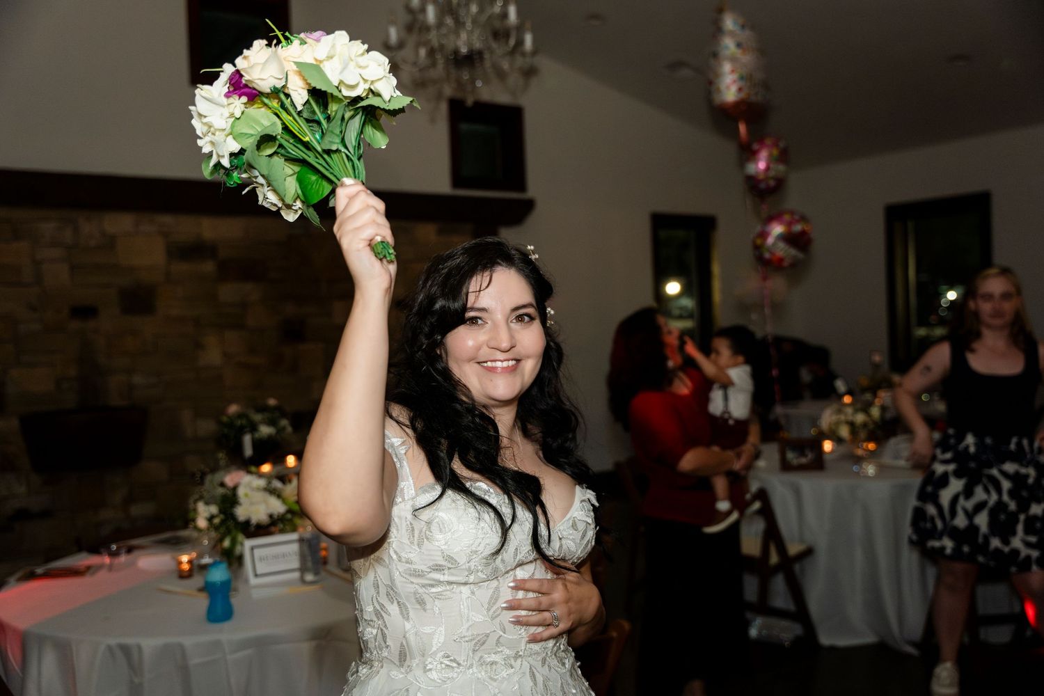 A joyful celebration at an indoor wedding reception venue with a white bouquet being held up in the air.
