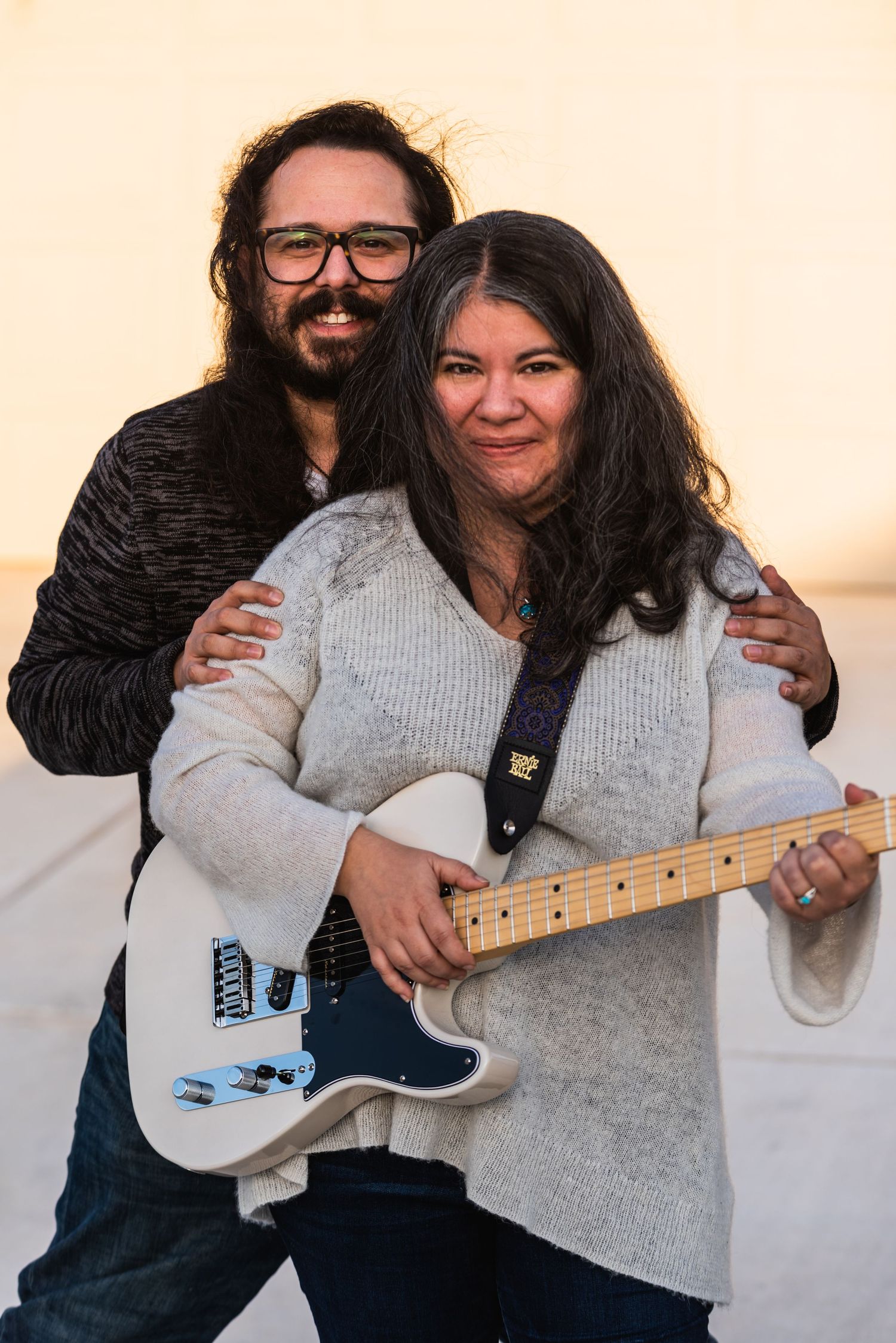 A happy couple poses together with a white electric guitar during their engagement.