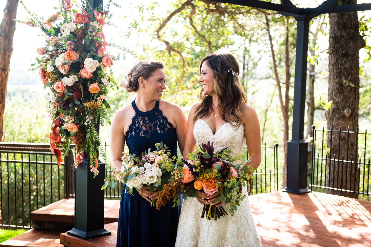 Two people sharing a joyful moment under a floral arch at an outdoor wedding venue.