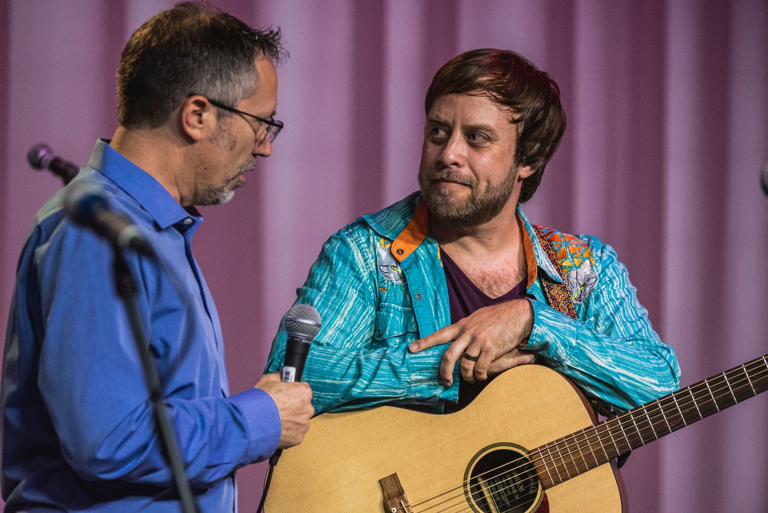 Interview with acoustic guitarist wearing turquoise shirt on stage.