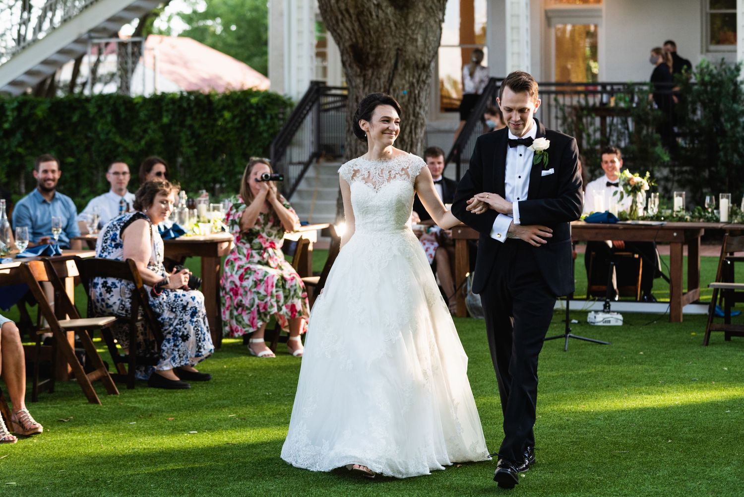 Couple walks down outdoor aisle together during elegant garden ceremony.
