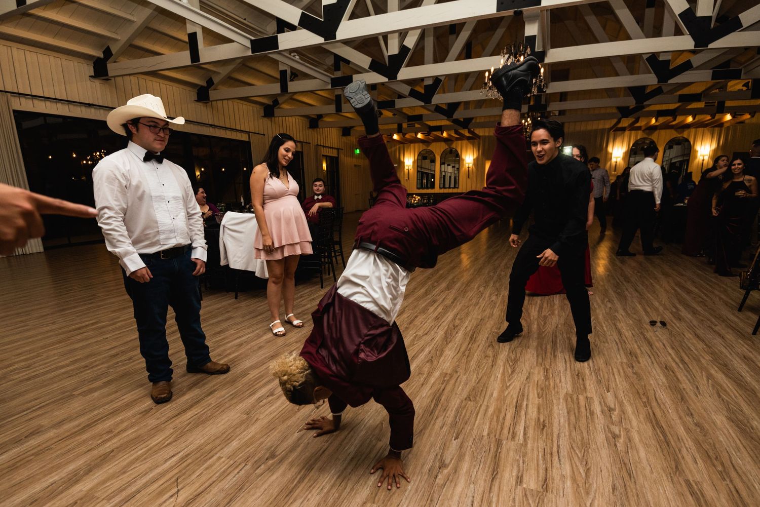 Guest performing breakdance moves on wooden dance floor at wedding reception.