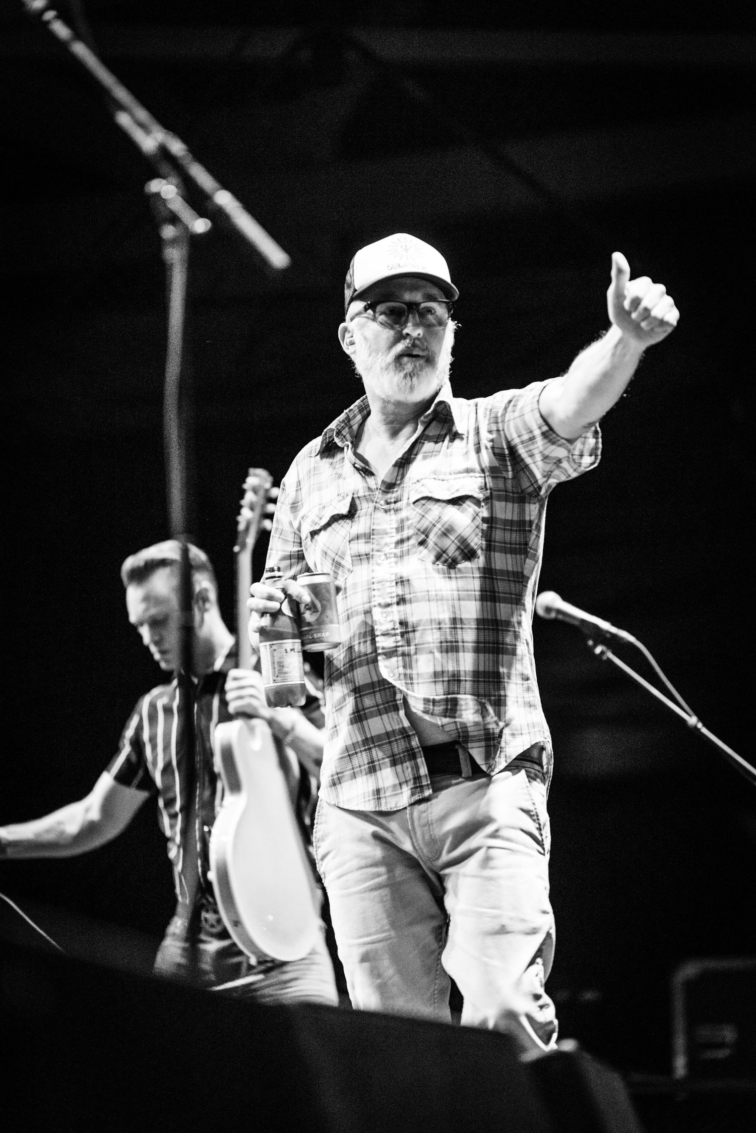 Black and white concert photo showing performer gesturing on stage with musicians in background.
