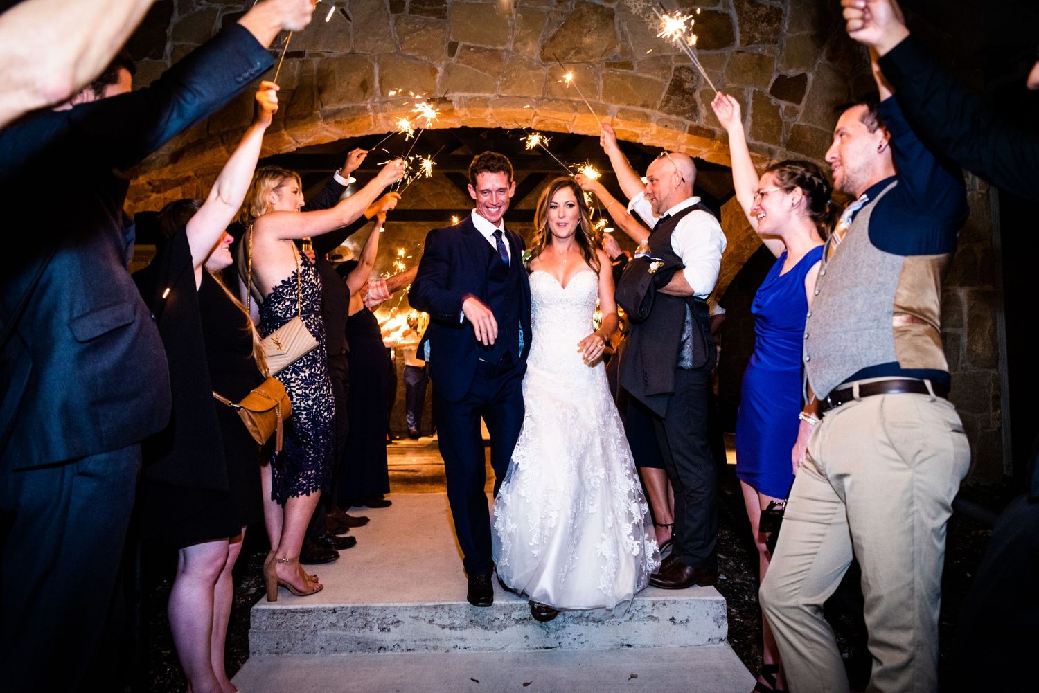 Wedding party creates a sparkler tunnel in a rustic stone venue for the couple's grand exit.