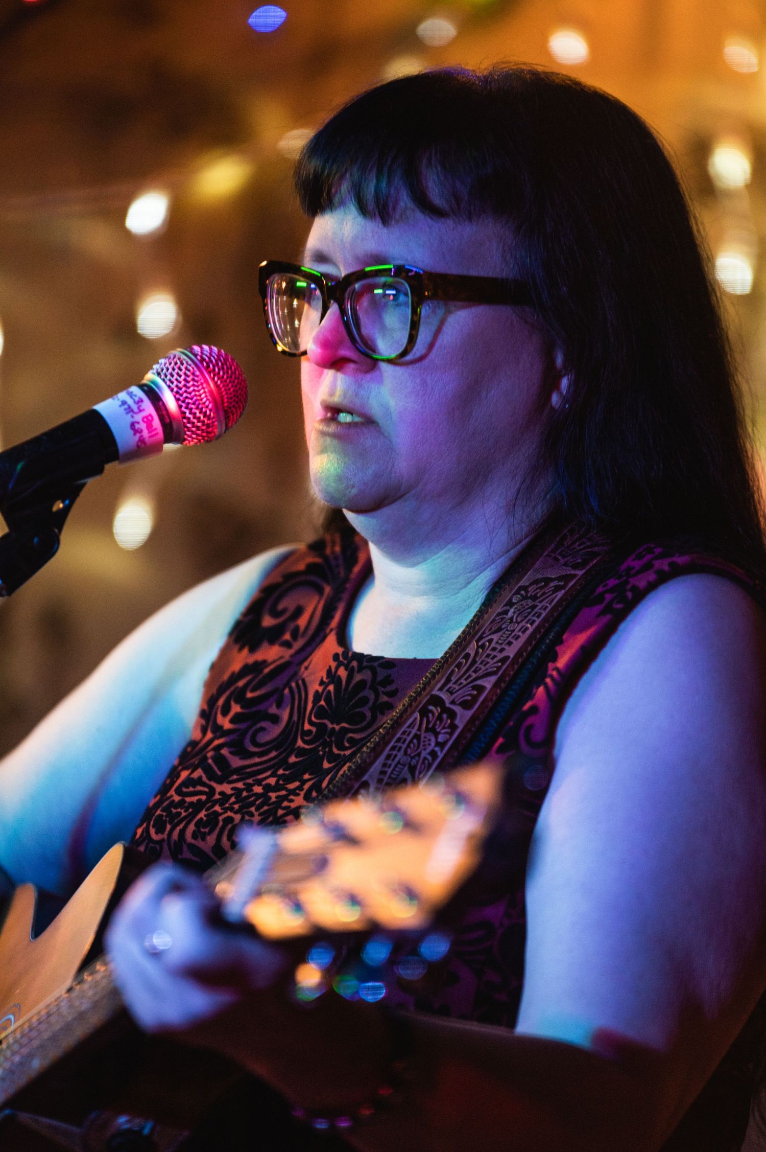 Concert performer singing into microphone while playing acoustic guitar under stage lights.