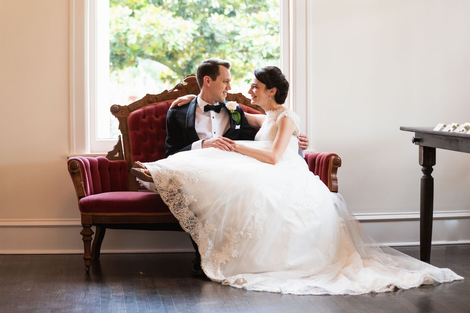 An intimate wedding moment captured on a vintage red velvet settee in an elegant indoor setting.