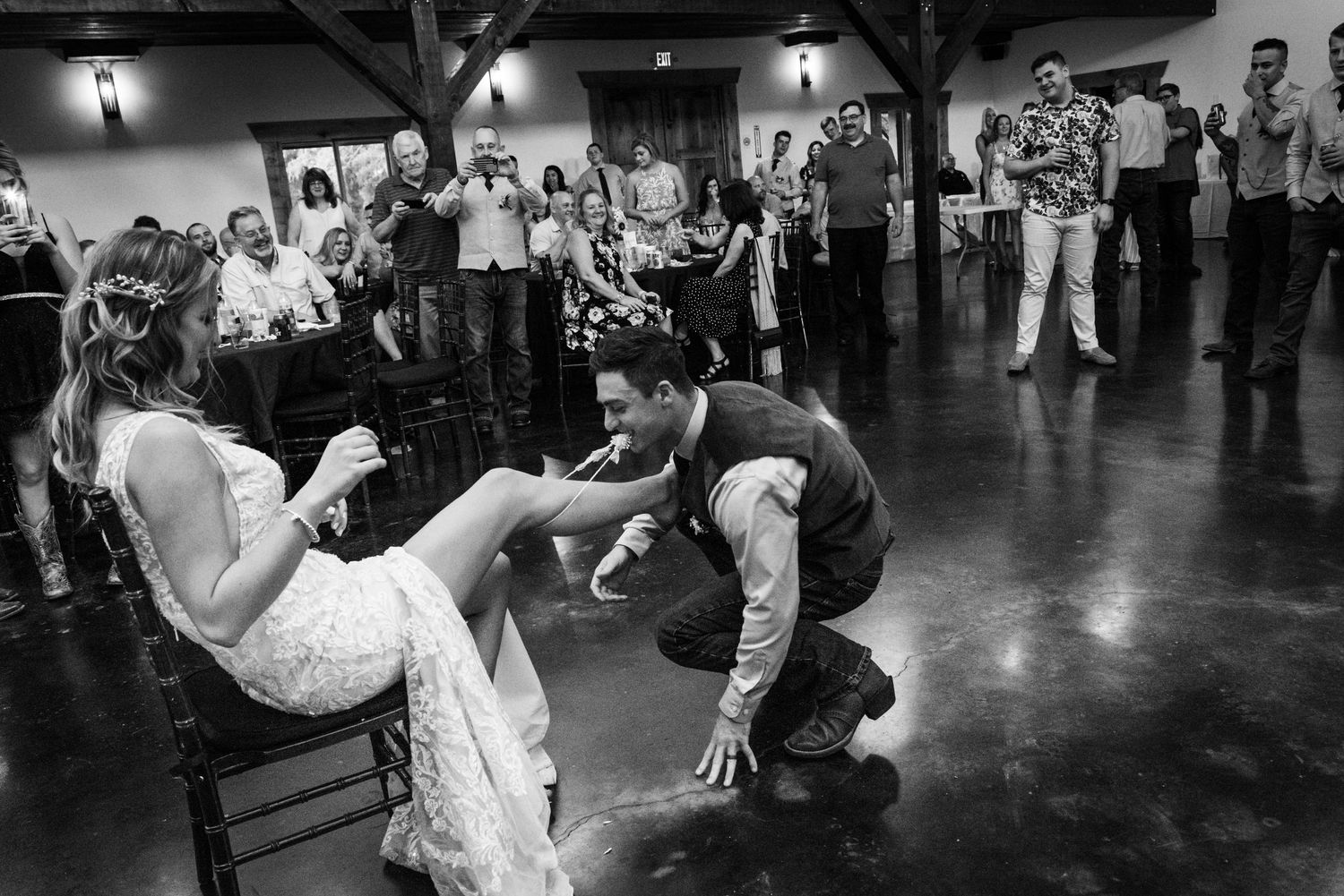 Black and white photo of wedding garter removal tradition at indoor reception.