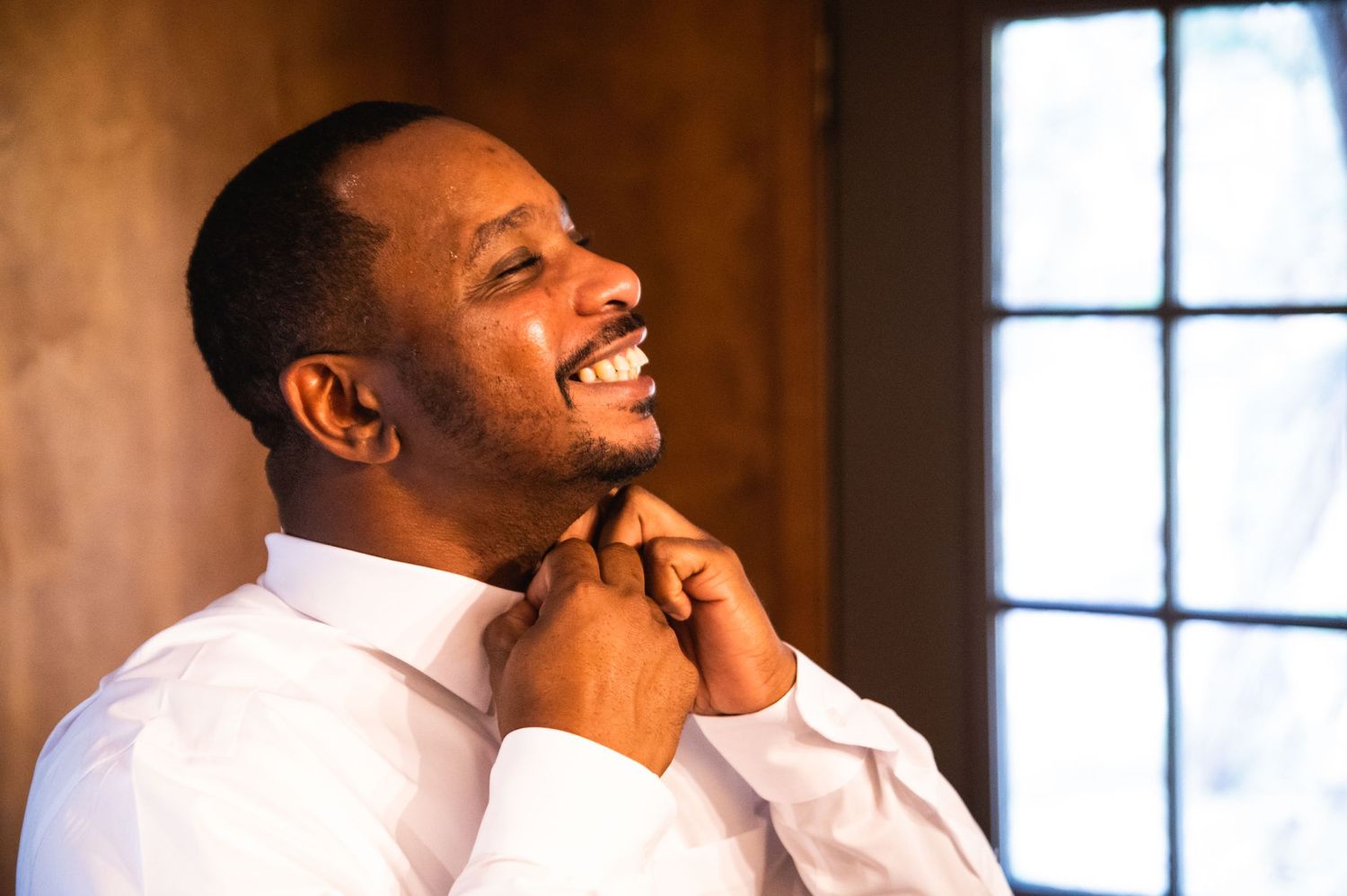 Person in white dress shirt adjusting tie with joyful expression.