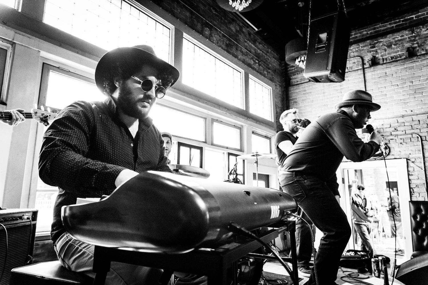 Musicians performing energetically in a brick-walled venue with dramatic black and white lighting.