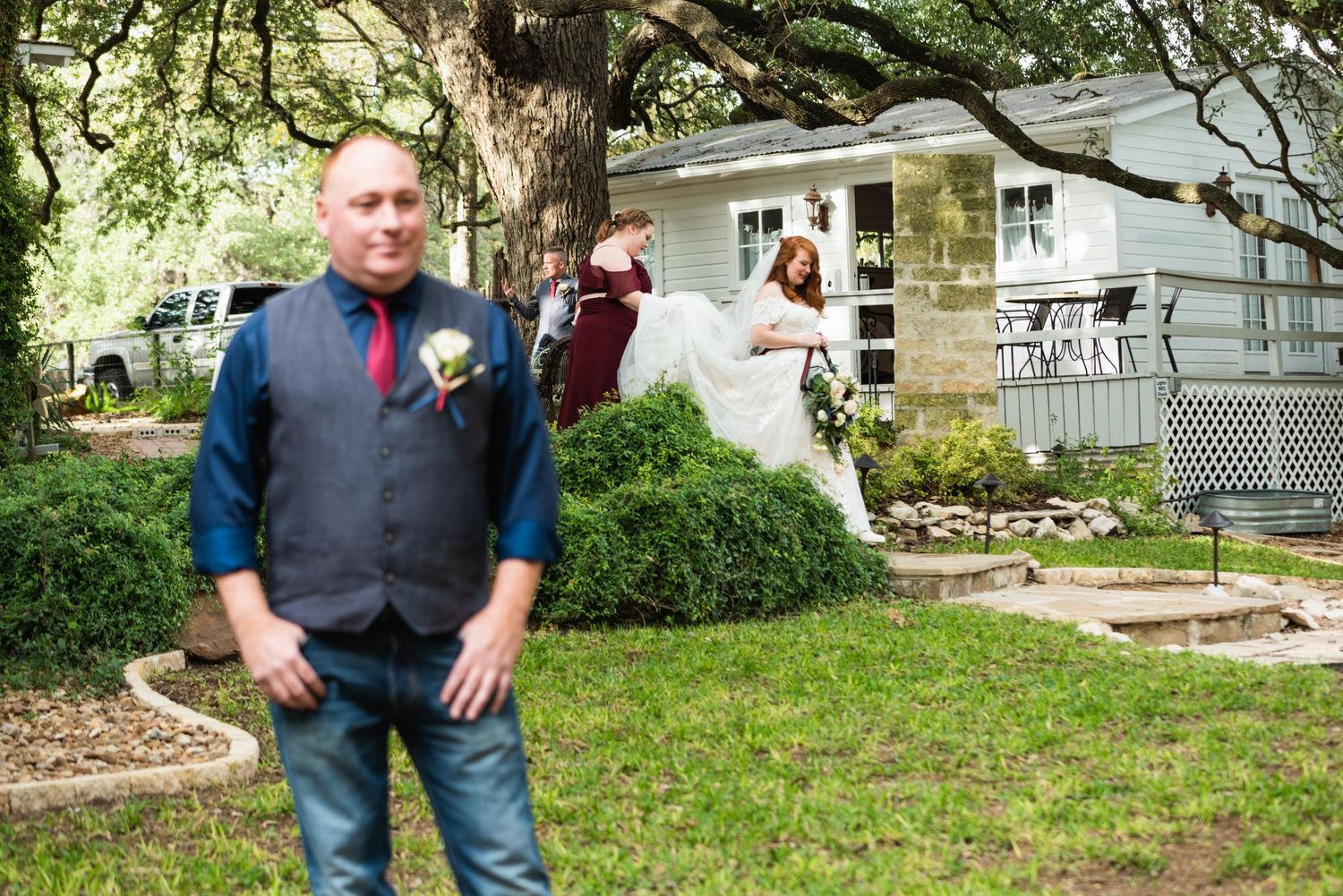 First look wedding photo with groom in foreground and bride in background by white house.