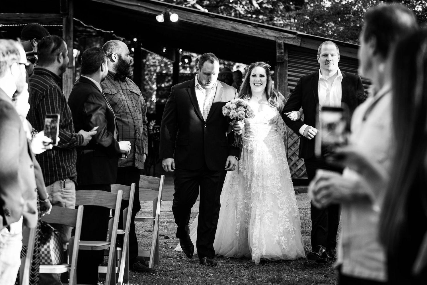 A black and white capture of a wedding ceremony processional with guests looking on.