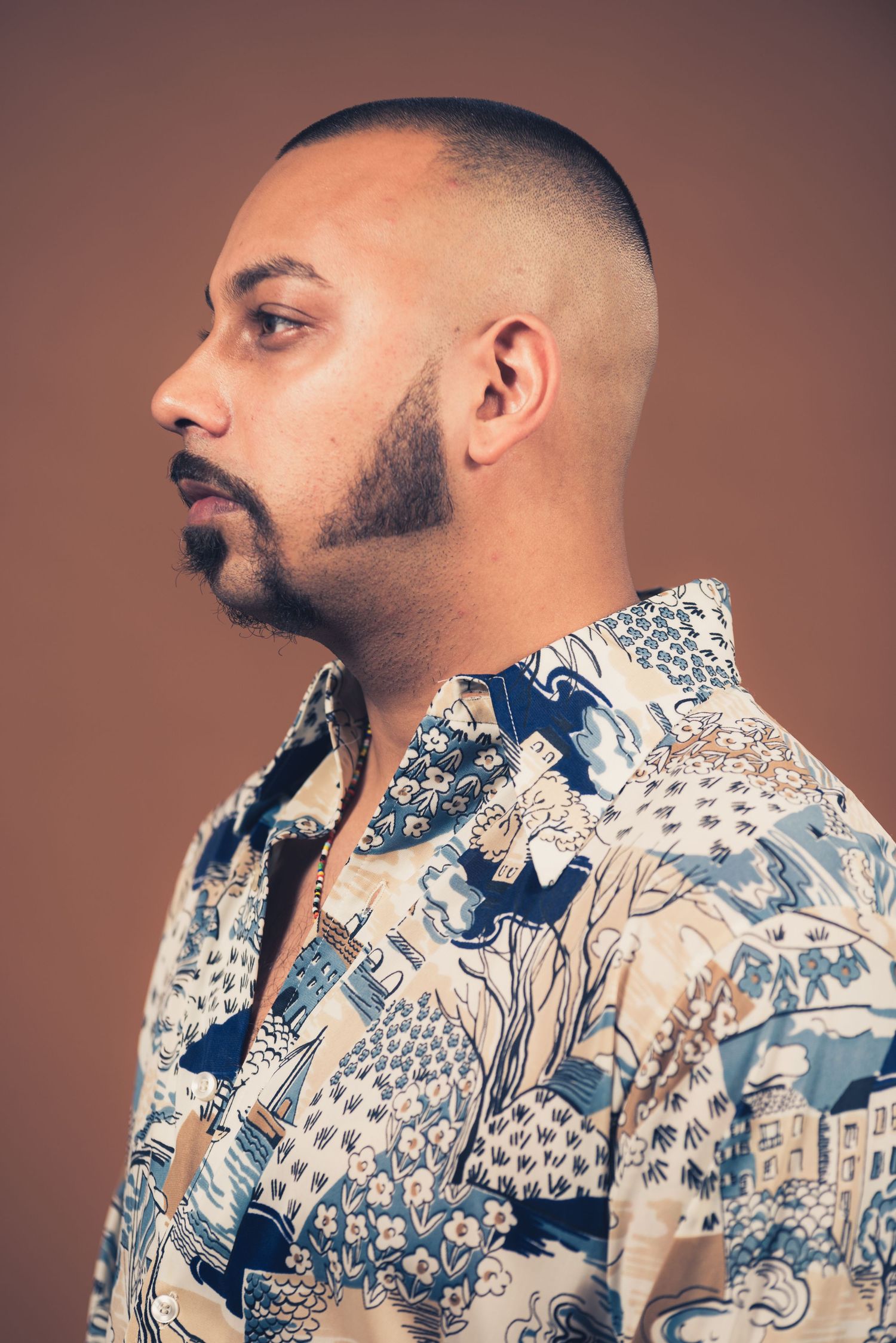 Side profile portrait of person in patterned shirt against brown backdrop.