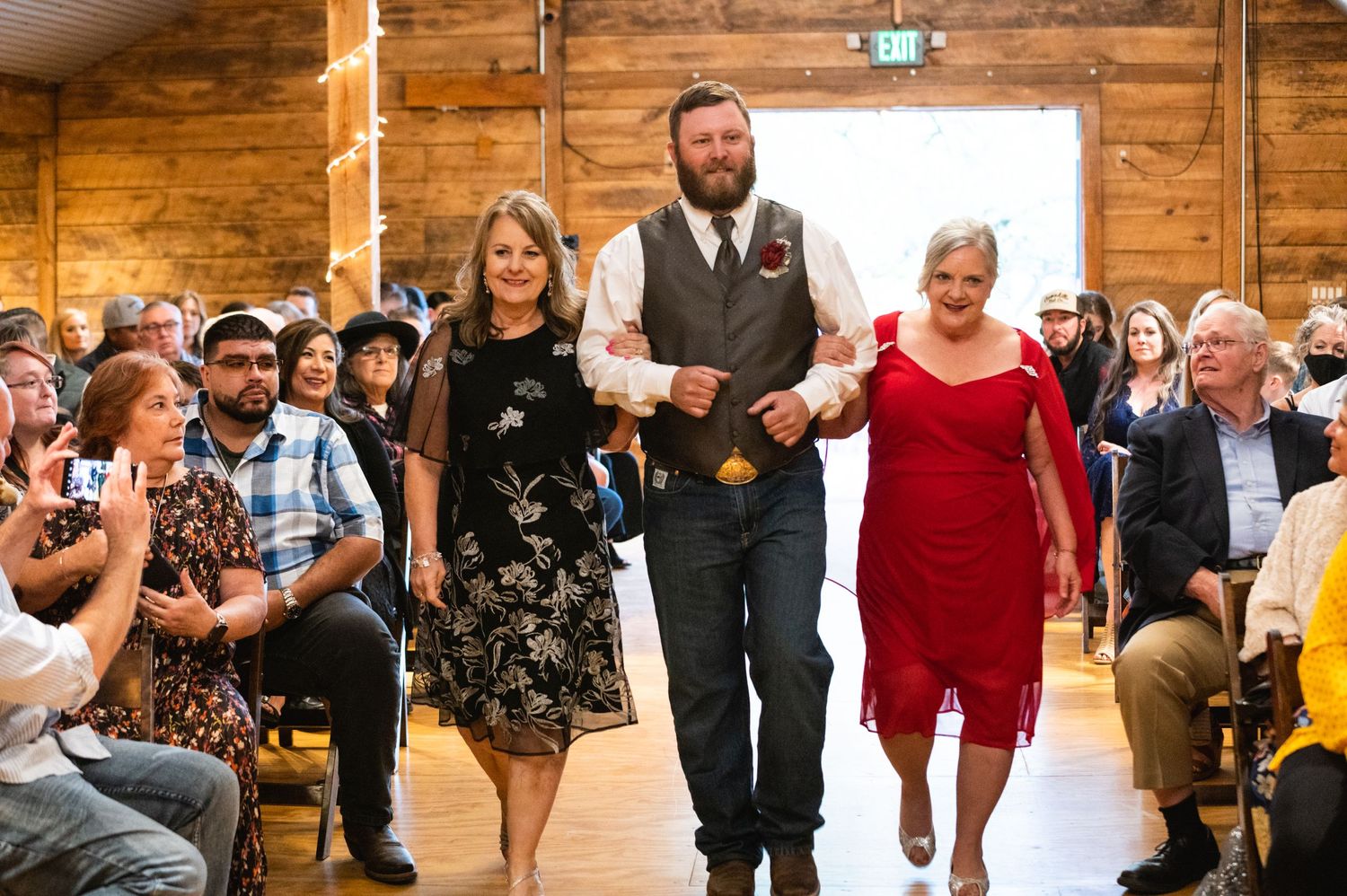 Wedding ceremony processional in a rustic wooden venue with guests looking on.