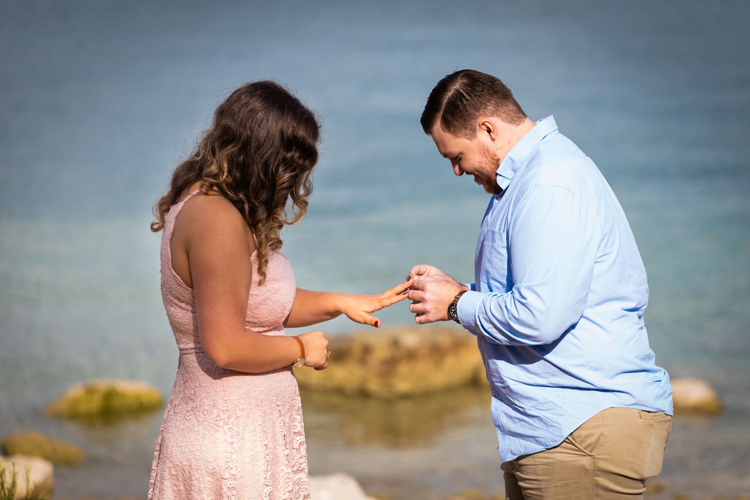 A couple shares an intimate moment as they examine a ring by the ocean.