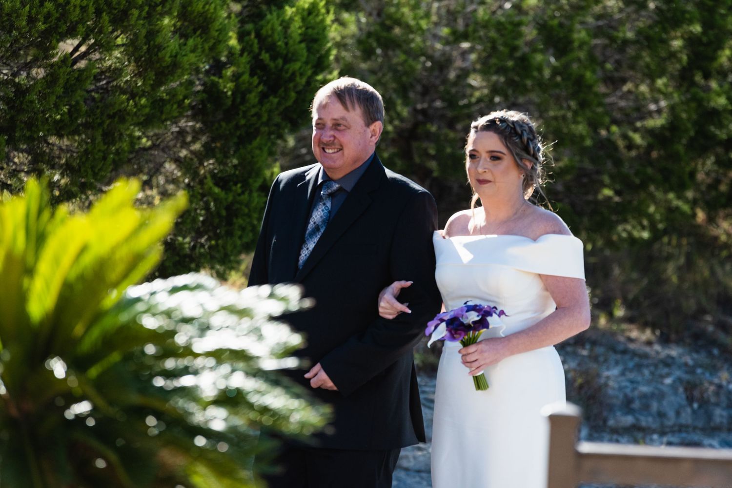 Outdoor wedding ceremony with stone wall and tropical foliage in background.