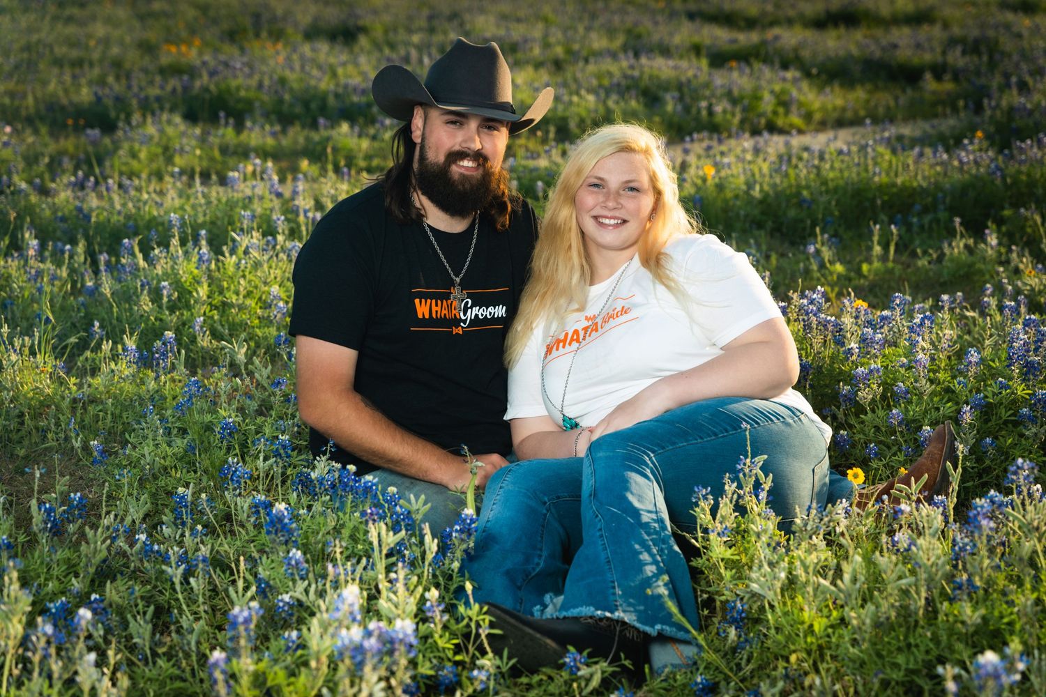 Couple sitting together in field of bluebonnets during sunset golden hour.