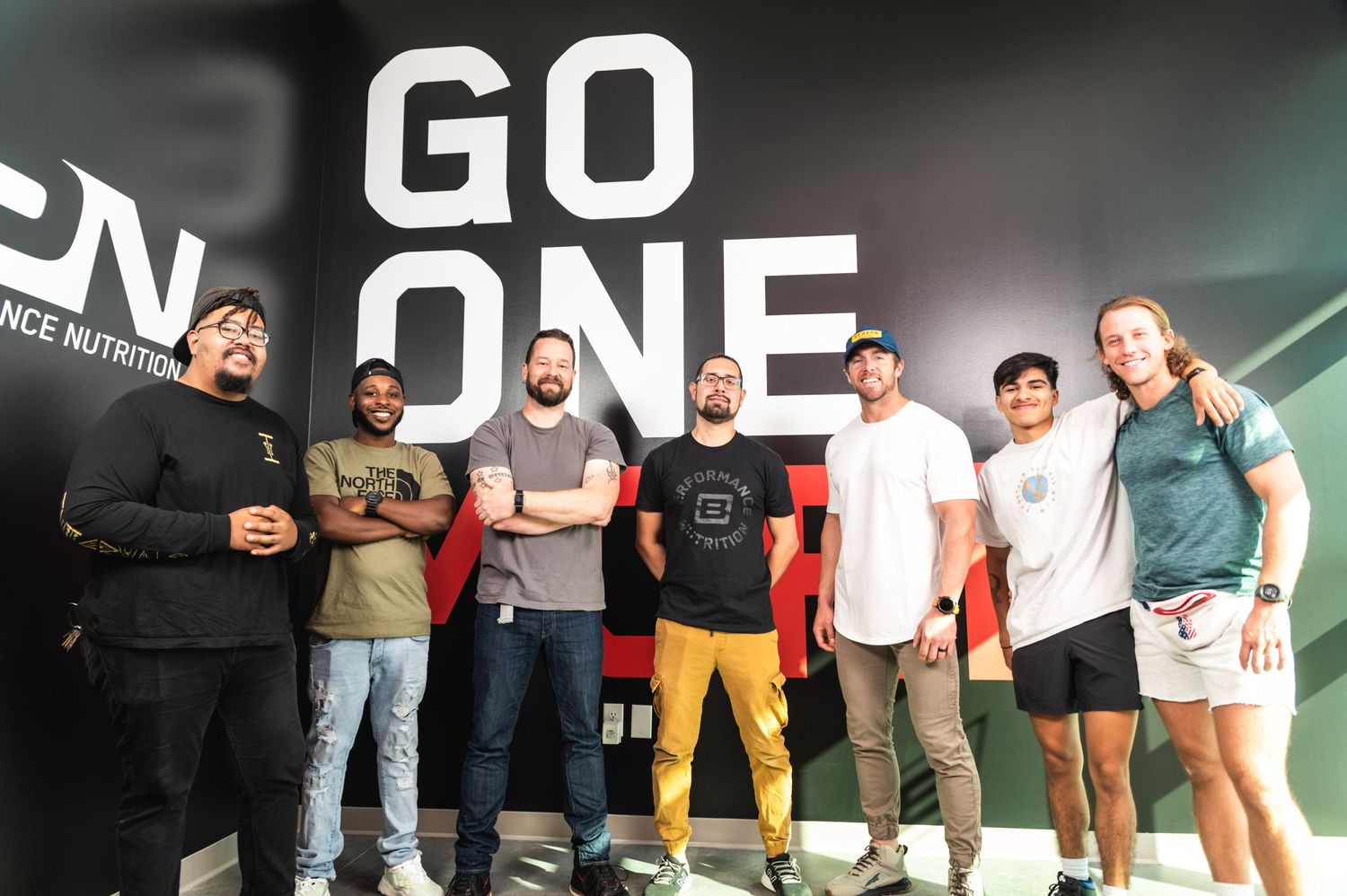 Group photo of fitness team posing in front of GO ONE wall signage.