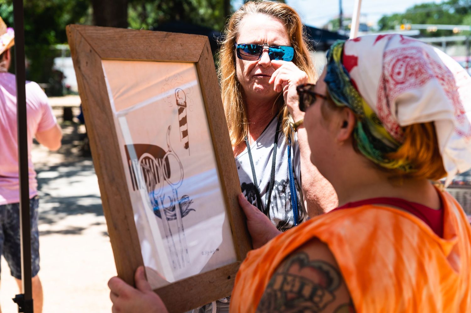 Two people examining artwork at an outdoor vendor booth.