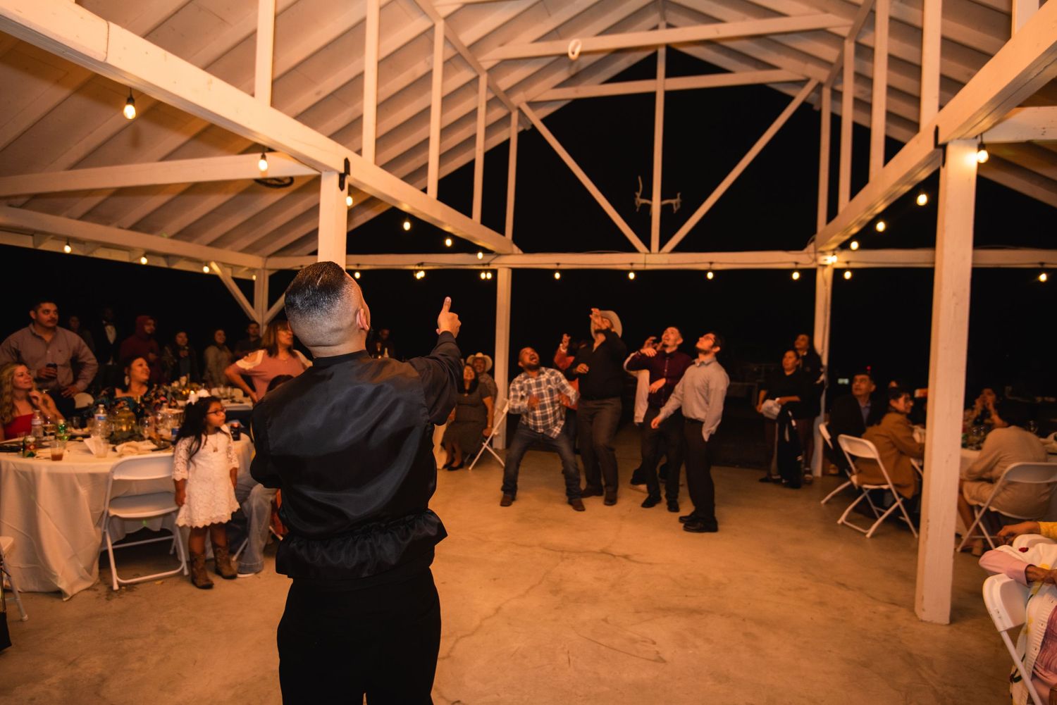 Reception venue with wooden beams and string lights as guests celebrate on the dance floor.