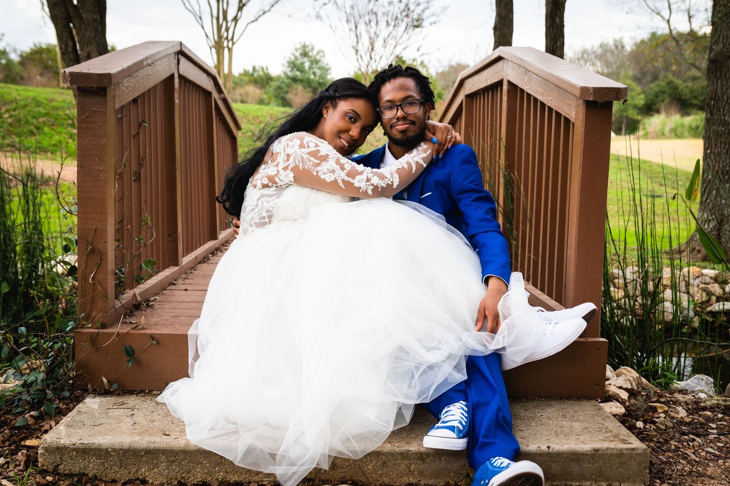 Newlyweds share intimate moment while sitting together on wooden bridge in wedding attire.