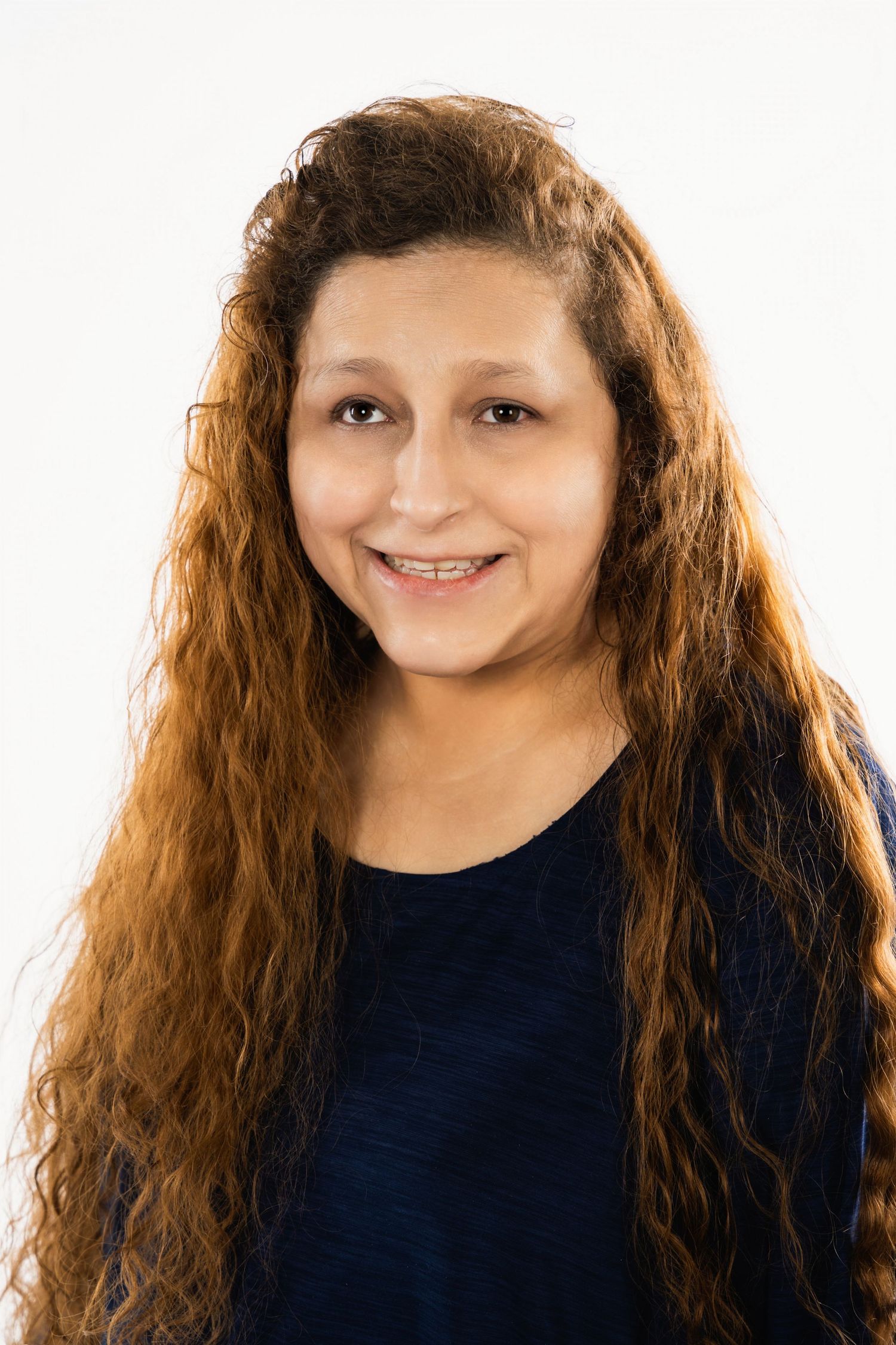 Portrait of someone with long wavy brown hair wearing a navy blue top against a white background.