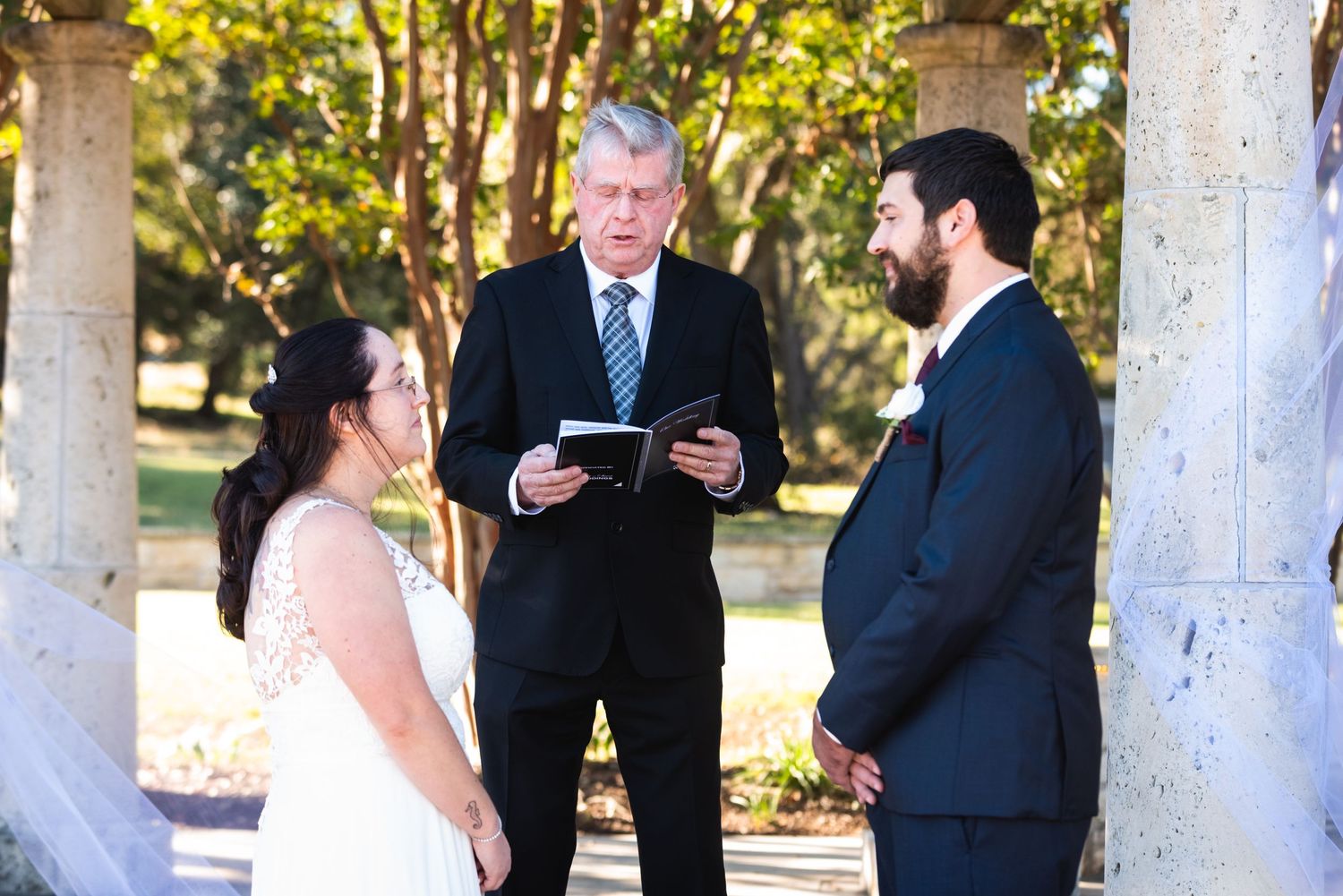 An outdoor wedding ceremony with stone columns and natural lighting.