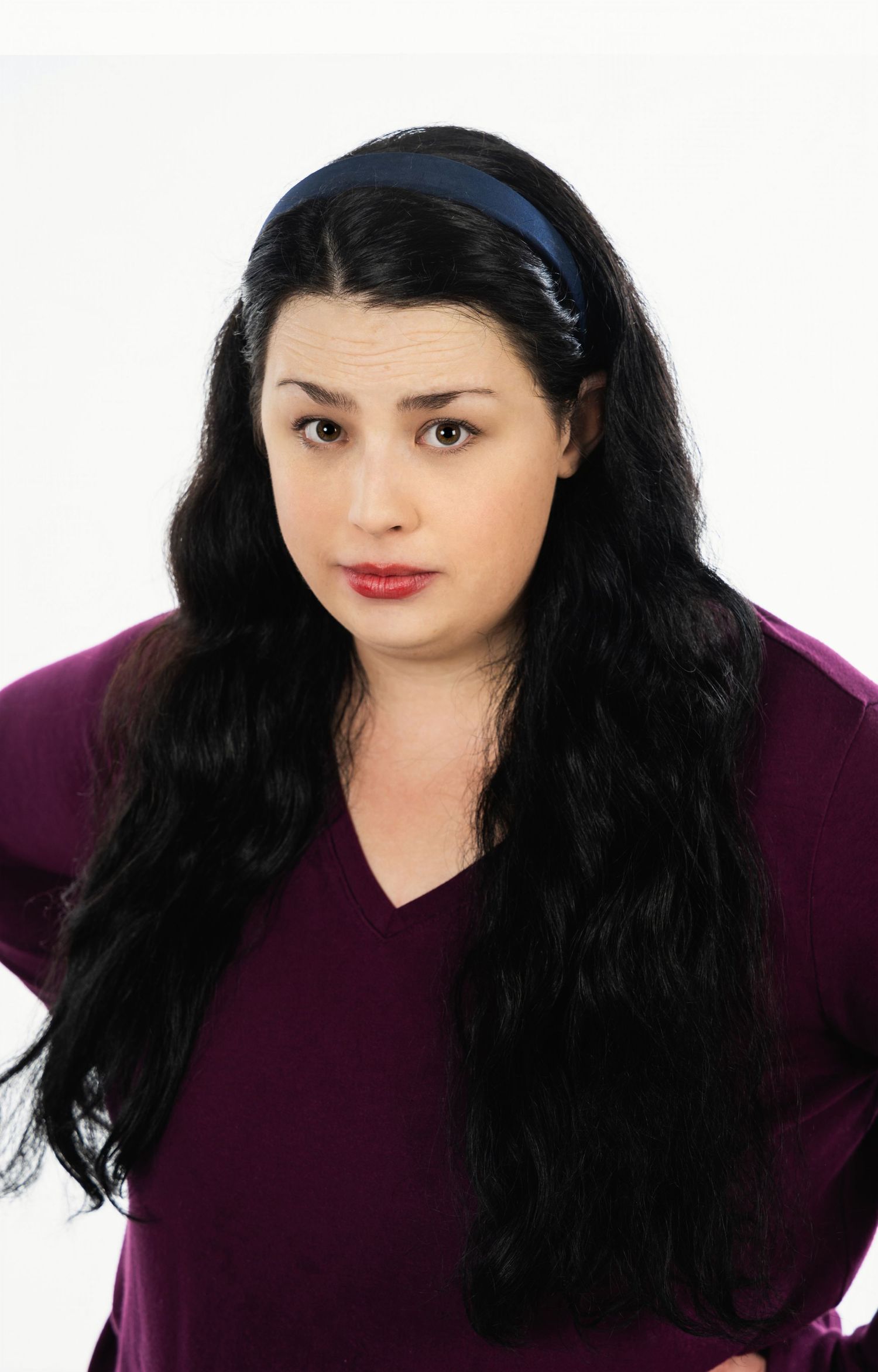 Studio portrait with long dark hair wearing purple top and headband against white background.