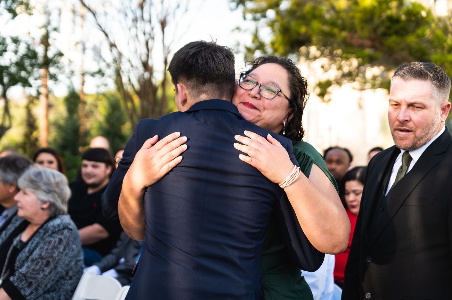Emotional embrace during outdoor wedding ceremony as guests look on.