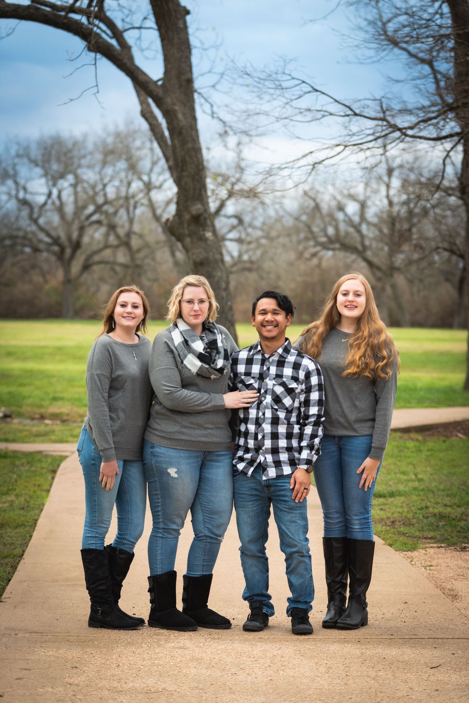 Four people in coordinated casual wear standing on concrete path with bare trees in background.