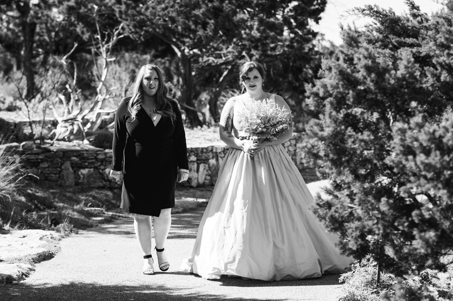 A black and white photo shows two people walking outdoors, one wearing a formal wedding gown.