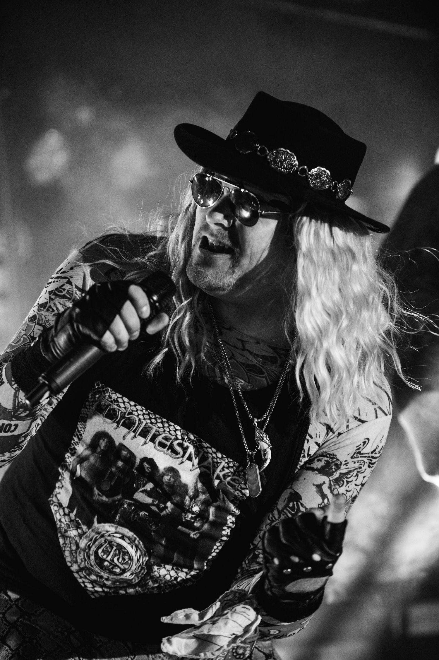 Singer performs on stage wearing cowboy hat, sunglasses and band t-shirt under dramatic lighting.