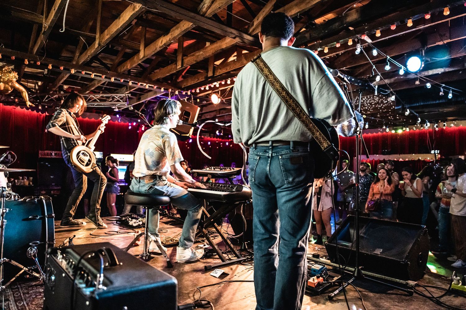 Rock band performs energetically on stage with dramatic lighting in a crowded venue.