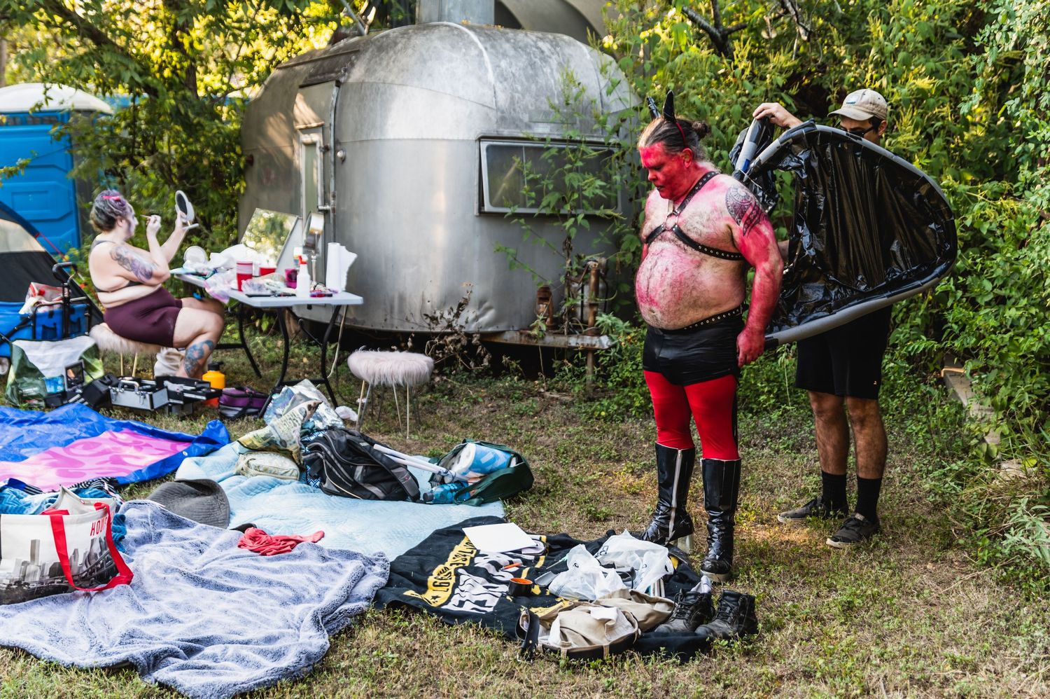 Two people in costumed attire standing near a silver airstream trailer with gear scattered around.