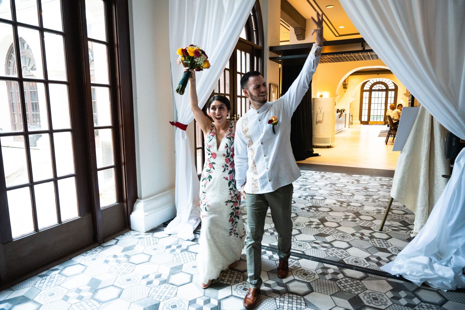 Couple celebrates joyfully behind sheer curtains in an elegant venue with ornate tile flooring.