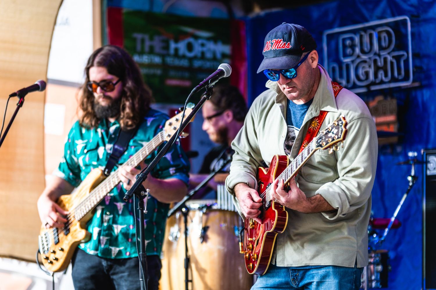 Musicians perform on stage with guitars at a live concert venue with Bud Light signage visible.
