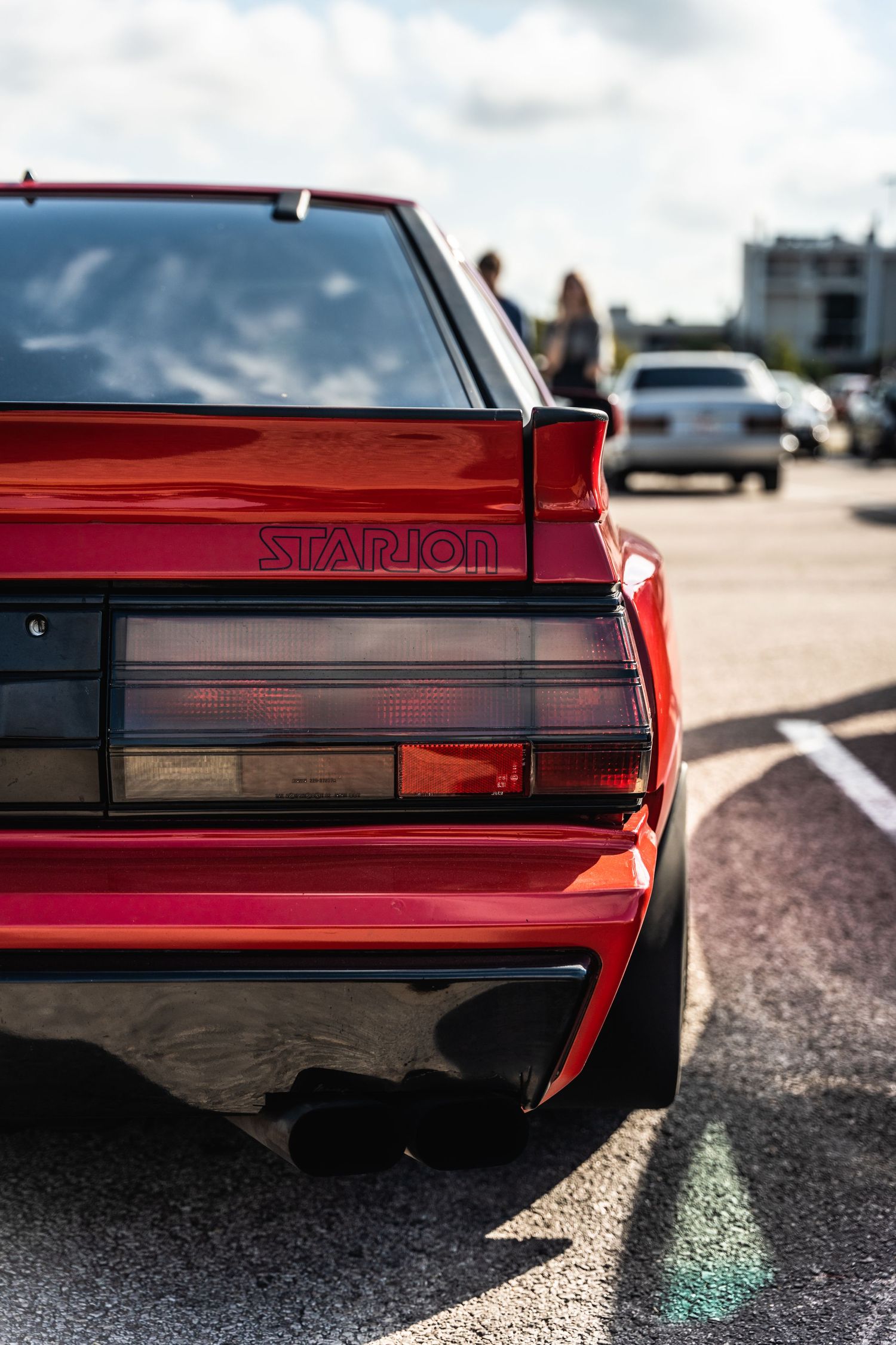 Close-up view of a red Starion sports car's rear quarter panel and taillights in a parking lot.