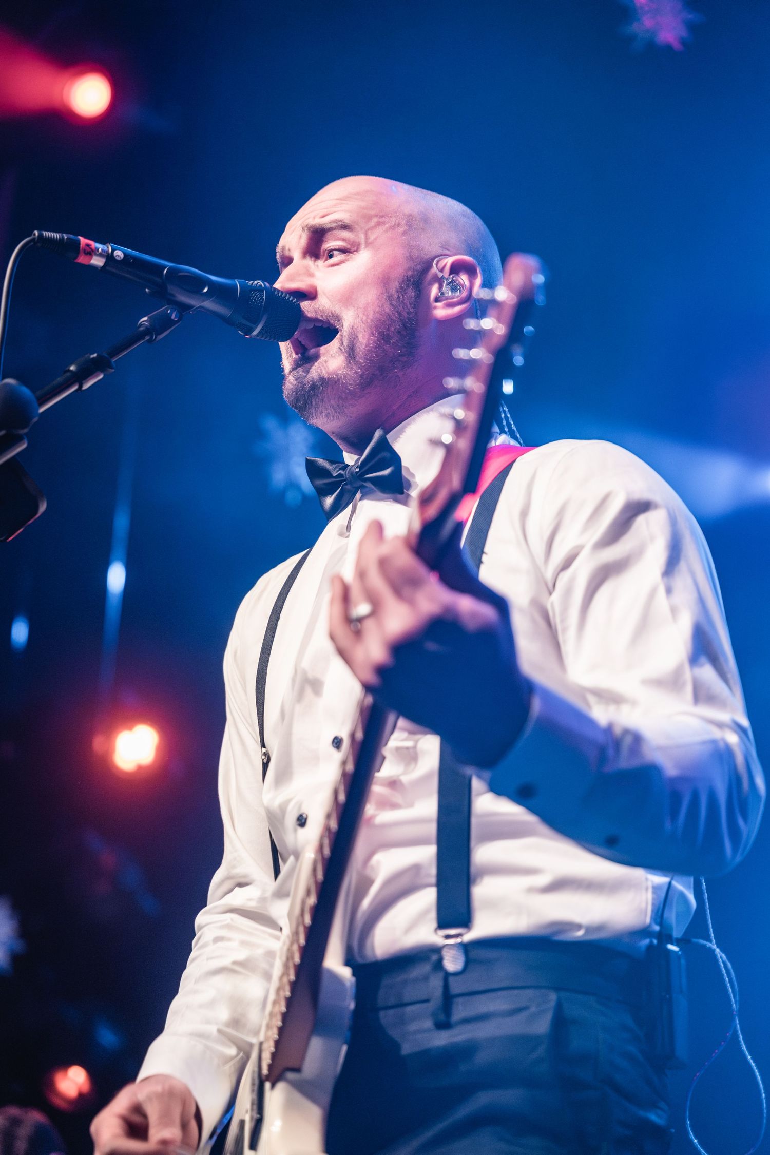 Musician in white shirt and bow tie singing passionately while playing guitar on stage.