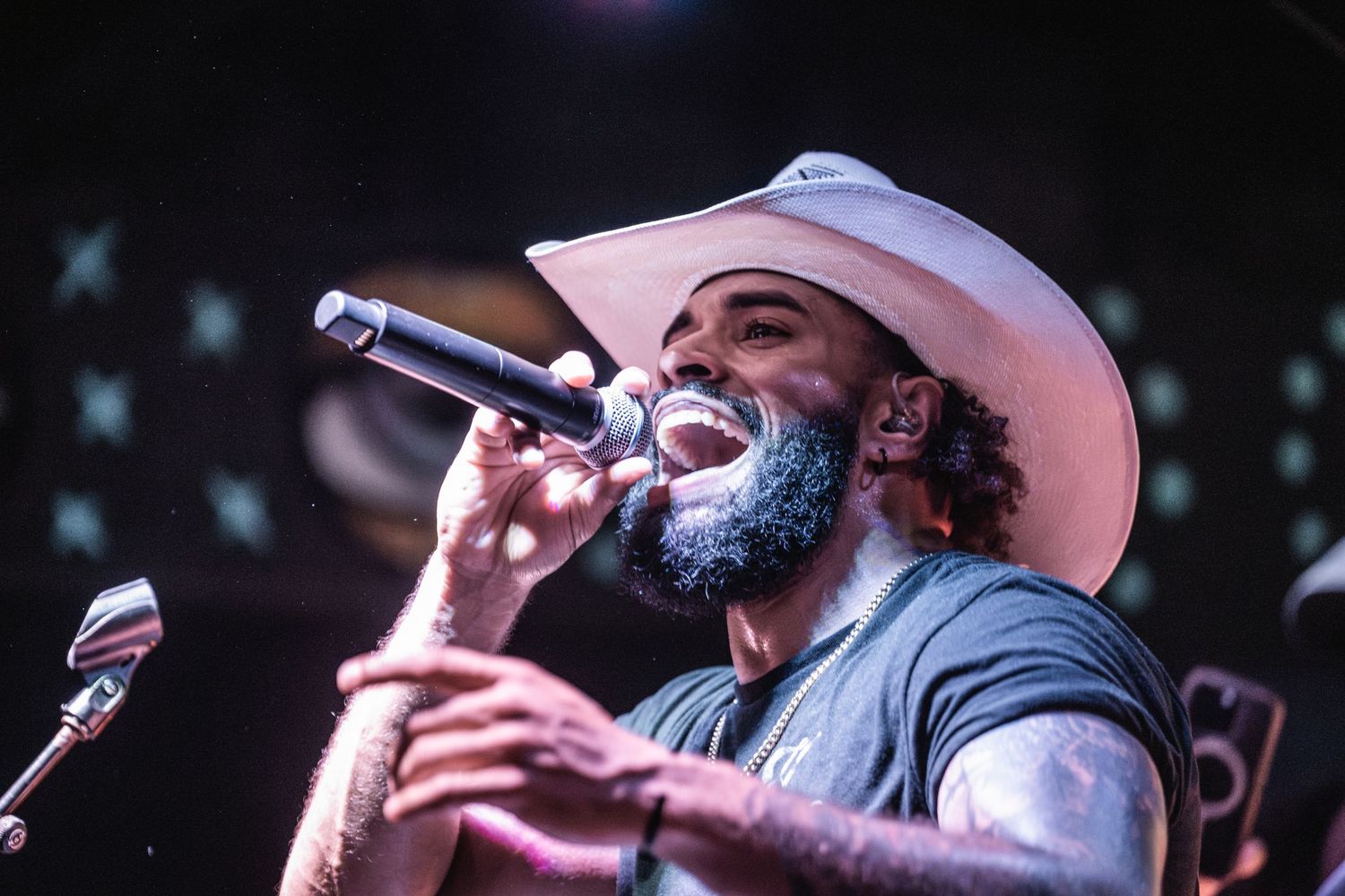 Country music singer wearing a cowboy hat performs passionately with microphone on stage during a live concert.