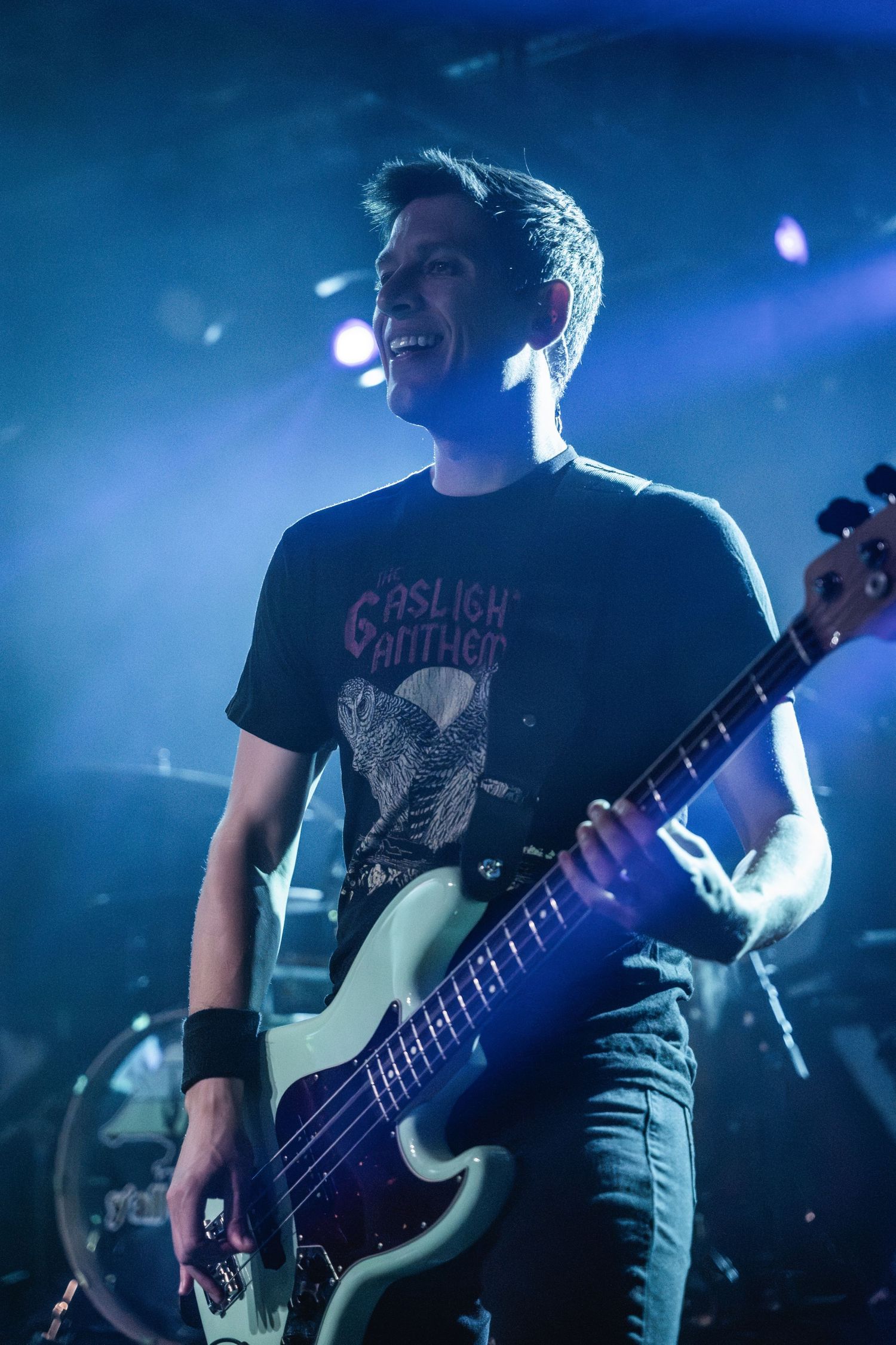 Bass player performing live wearing a band t-shirt under blue stage lighting.