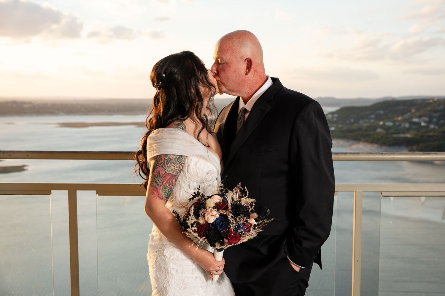 Intimate wedding moment captured on balcony overlooking water at dusk.