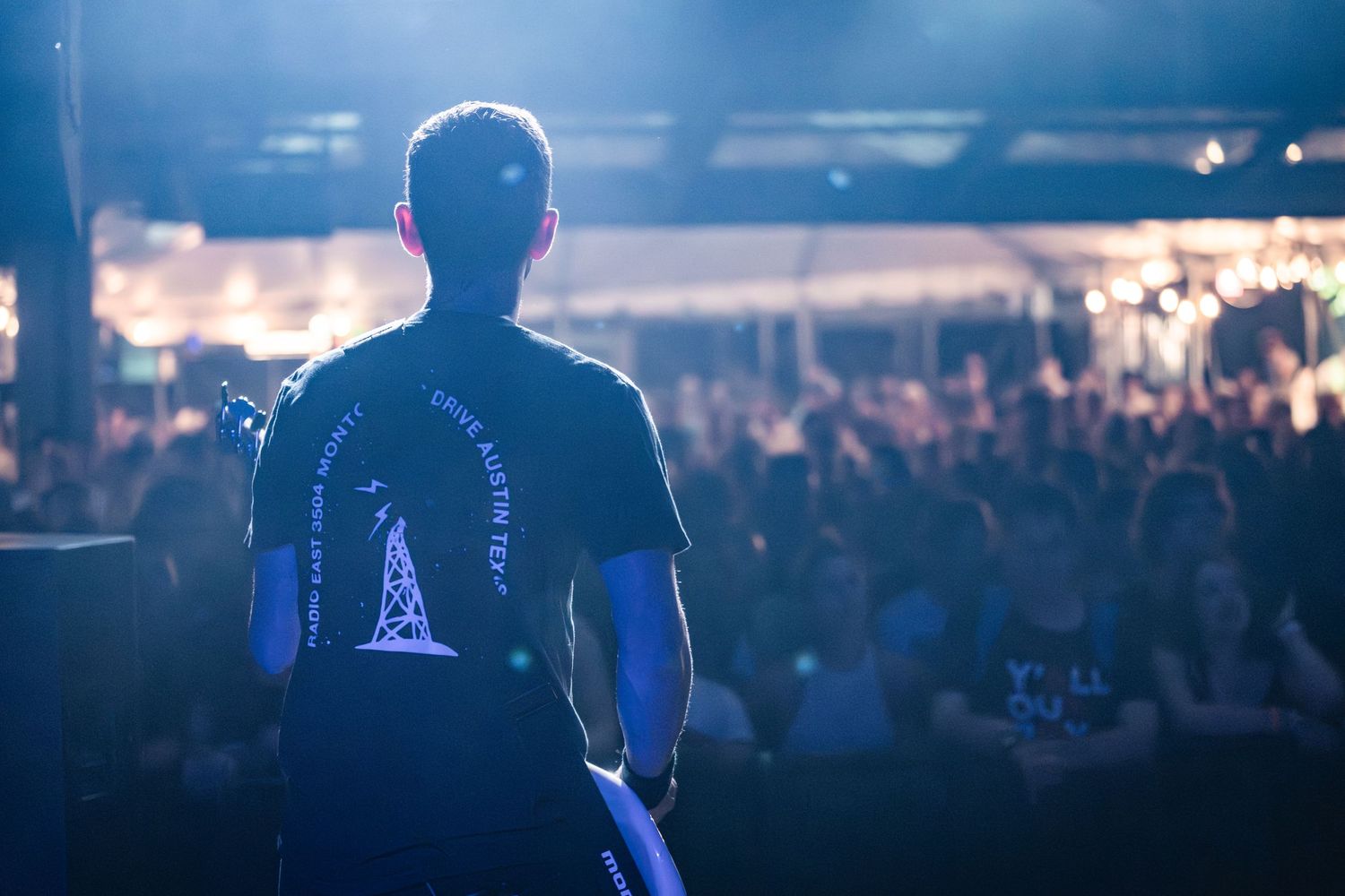 Silhouette of performer on stage looking out at large concert crowd.